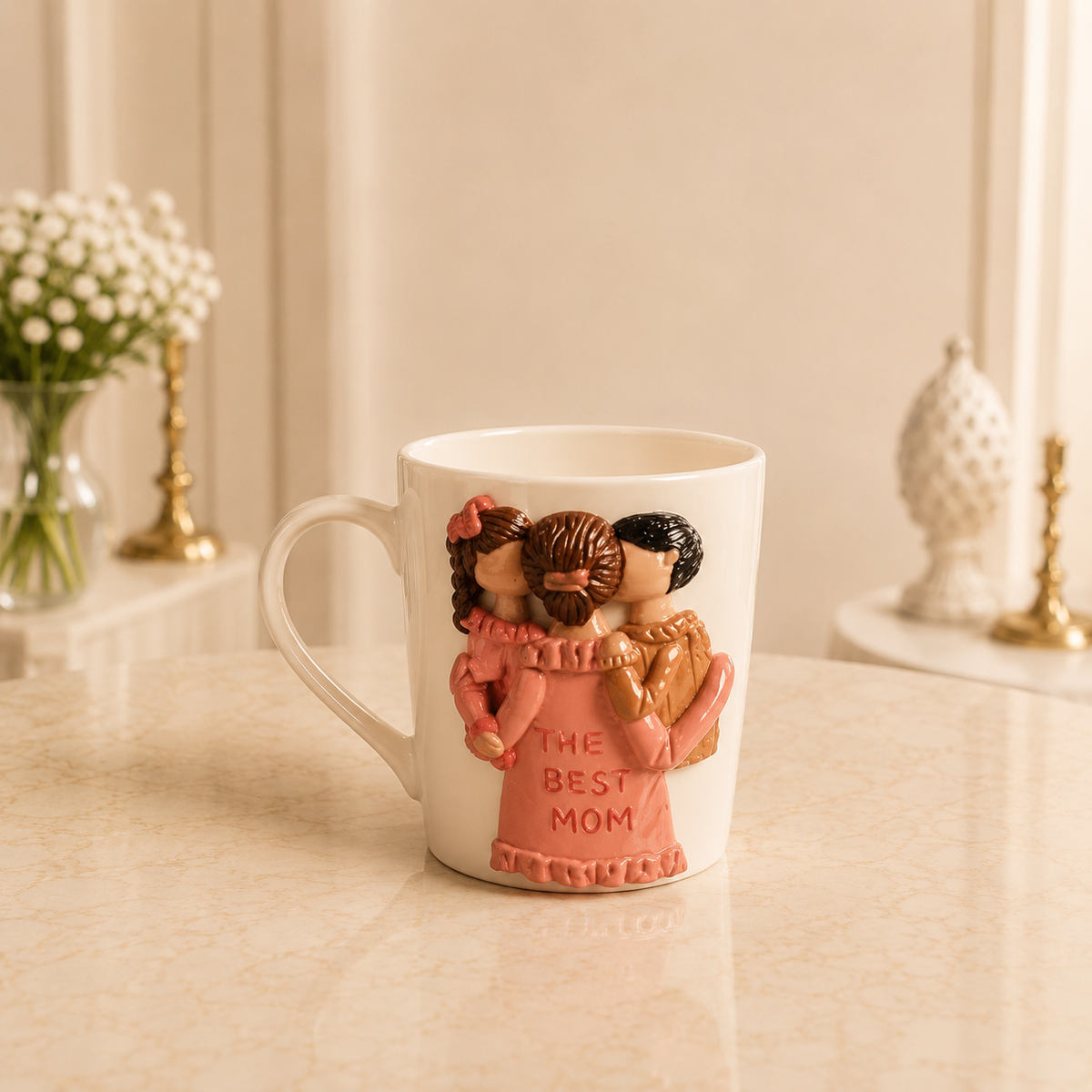 Blush Cradle Mug - white ceramic mug sculpted with a mother in a salmon pink dress lettered THE BEST MOM holding a baby