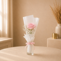 Blush Solitaire - a single pale pink rose with baby's breath in white wrap tied with a pink ribbon, standing in a small clear glass vase